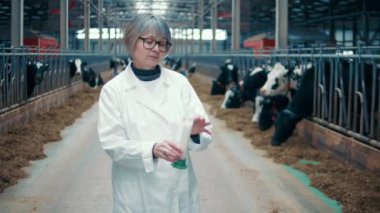 Female worker is smelling fresh milk in the cowshed. 4K