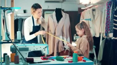 Female designer and her daughter are measuring a mannequin. 4K