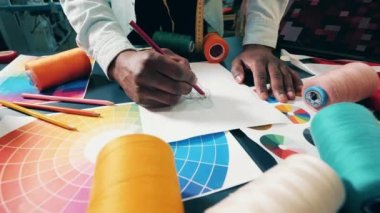 African dressmaker is sketching a dress on his desk. 4K