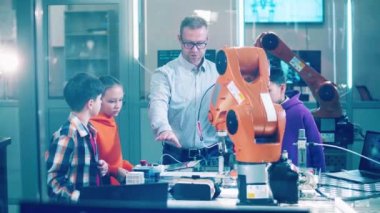 Children and a male engineer are observing a robotic arm. 4K
