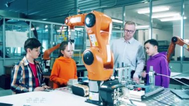 Male engineer and children are watching a robotic arm in motion. 4K