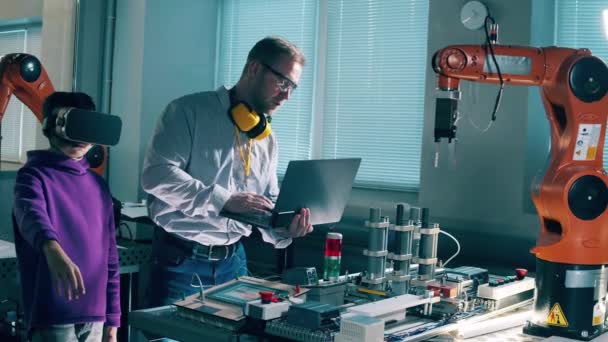 Инженер Мужчина Помогает Мальчику Очках Управлять Роботизированной Рукой — стоковое видео
