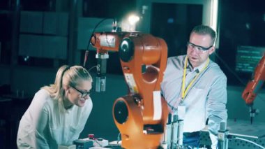 Two engineers are watching a robotic arm with interest. 4K