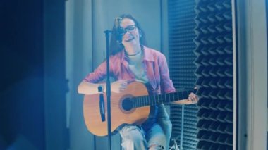 Recording booth with a woman singing and playing the guitar. 4K