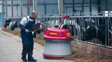 Cattle farmer is controlling a machine pushing hay to the cows. 4K
