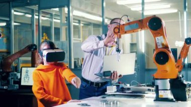 Male tutor is monitoring a girl in VR-glasses operating a robot. 4K