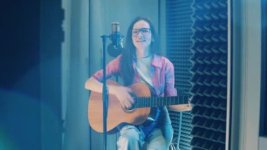 Recording booth with a female musician playing the guitar. 4K