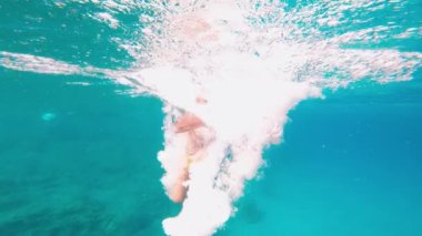 Havuzun içinden, genç beyaz çocuk havuza atlıyor ve yüzme gözlükleriyle dalıyor. 7 yaşında bir çocuk güneşli ve bulutlu bir günde yazın yüzüyor ve eğleniyor. Tatil konsepti. 4K