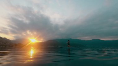 Yazın günbatımında SUP sörf yaparken tanınmayan genç bir kadın. 4K