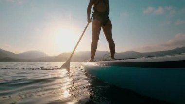 Yazın günbatımında SUP sörf yaparken tanınmayan genç bir kadın. 4K