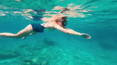 Suyun altında şnorkelle yüzen bir kız. Mayolu bir kadın denizin dibinde serbest dalış yapıyor. 4K