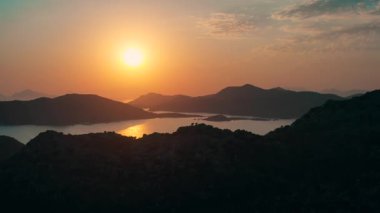 Sakin sularda güzel bir şekilde parlayan, nefes kesici bir gün batımı. Uzaktaki siluetli dağlarla birlikte.
