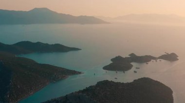 Güneşin puslu batışında sakin suların yanında güzel adaları esir alan çarpıcı ve huzurlu bir hava görüntüsü.