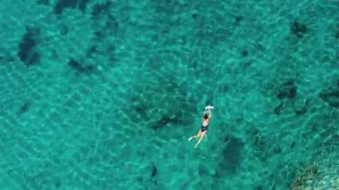 Sakin bir hava manzarası canlı turkuaz suların ve büyüleyici deniz yaşamının tadını çıkaran bir şnorkelçiyi gösteriyor.