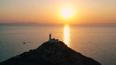 Kayalık bir sahil şeridindeki deniz fenerinin çarpıcı günbatımı manzarası okyanusa güzel yansımalar yansıtıyor.