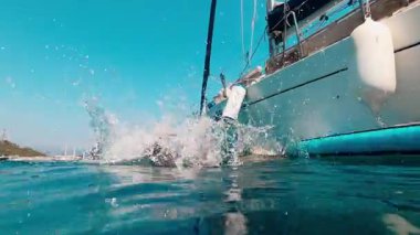 Renkli bir yelkenlinin yanında berrak sularda bir çocuk raket, yaz eğlencesi ve macerayı simgeliyor.