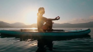 Suyun üzerinde yüzerken huzurlu bir meditasyon anı güzel bir günbatımı boyunca raket 4K üzerinde.