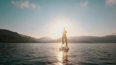 Huzurlu bir gün batımı, sakin bir gölün üzerinde zarif bir şekilde kürek çekerken mükemmel güzelliğini yakalar.