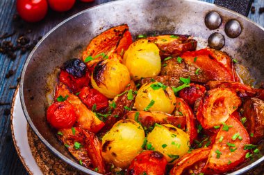 Ahşap masa üzerinde kavrulmuş kiraz domatesleri dökme demir tavada.