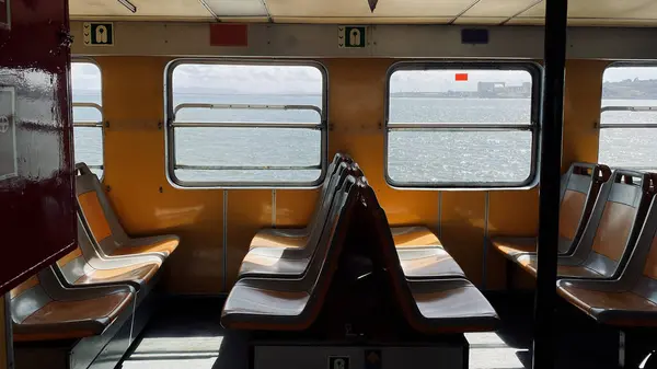 Boş eski yolcu feribotu, parlak sarı güneşli iç mekan, boş eski koltuklar, açık pencerelerin arkasında nehrin geniş mavi suyu..