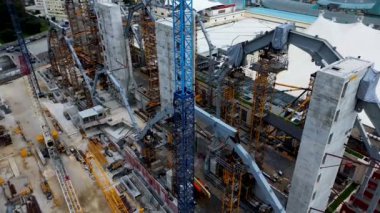 Büyük yapıları, inşaat ekipmanları, vinçleri ve kazıcıları olan bir inşaat alanı. Yüksek metal kemerleri ve beton yapıları olan bir bölge. Drone görünümü.