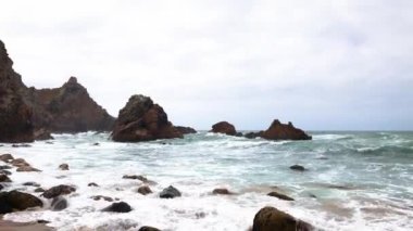 Kıyıya vuran dalgalarla birlikte kayalık sahil şeridi. Sarp kayalıklar ve dağınık kayalar bulutlu bir gökyüzünün altındaki deniz manzarasını çerçeveliyor. Kumsal. Atlantik Okyanusu. 