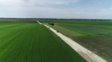 Toprak bir yolda yeşil ve siyah tarlalar arasında gidip gelen iki araba toz kaldırıyor. Yolculuklar. Drone. Hava görünümü.