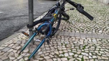 Eski terk edilmiş bisiklet iskeleti direğe kilitlenmiş, ön tekerlek çalınmış. Hasarlı bisiklet kaldırımda duruyor.. 