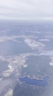 Uçak penceresinden çok sayıda göl, orman ve dolambaçlı yollarla manzaralı bir manzara. Uçak bulutlu bir gökyüzünün altında yüksek bir irtifada uçuyor..