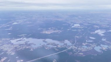 Uçak penceresinden çok sayıda göl, orman ve dolambaçlı yollarla manzaralı bir manzara. Uçak bulutlu bir gökyüzünün altında yüksek bir irtifada uçuyor..