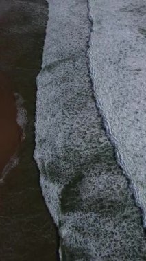 Kıyıya çarptıklarında okyanus dalgalarının yuvarlanan ve köpüren hava görüntüsü. Koyu yeşil su, beyaz köpüklü sörf, büyüleyici doğal doku. Yukarıdan güçlü bir deniz hareketi. İHA. 