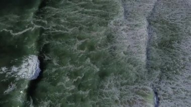 Kıyıya çarptıklarında okyanus dalgalarının yuvarlanan ve köpüren hava görüntüsü. Koyu yeşil su, beyaz köpüklü sörf, büyüleyici doğal doku. Yukarıdan güçlü bir deniz hareketi. İHA. 