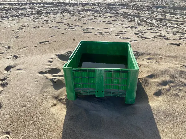Terk edilmiş yeşil balık plastik sandığı kumsalda. Gölgeler, güneş. Çekici tekerlek izleri, kumulları kaplayan ayak izleri..