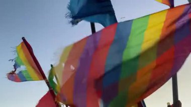 Yıpranmış deniz balıkçılığı sinyalleri canlı gökkuşağı renklerinde, LGBTQ + gurur bayraklarına benzeyen, alacakaranlıkta okyanus esintisinde dalgalanan. Dayanıklılık, kimlik ve kıyı geleneklerinin sembolü.