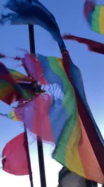 Yıpranmış deniz balıkçılığı sinyalleri canlı gökkuşağı renklerinde, LGBTQ + gurur bayraklarına benzeyen, alacakaranlıkta okyanus esintisinde dalgalanan. Dayanıklılık, kimlik ve kıyı geleneklerinin sembolü.