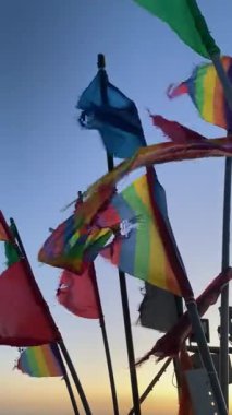 Yıpranmış deniz balıkçılığı sinyalleri canlı gökkuşağı renklerinde, LGBTQ + gurur bayraklarına benzeyen, alacakaranlıkta okyanus esintisinde dalgalanan. Dayanıklılık, kimlik ve kıyı geleneklerinin sembolü.