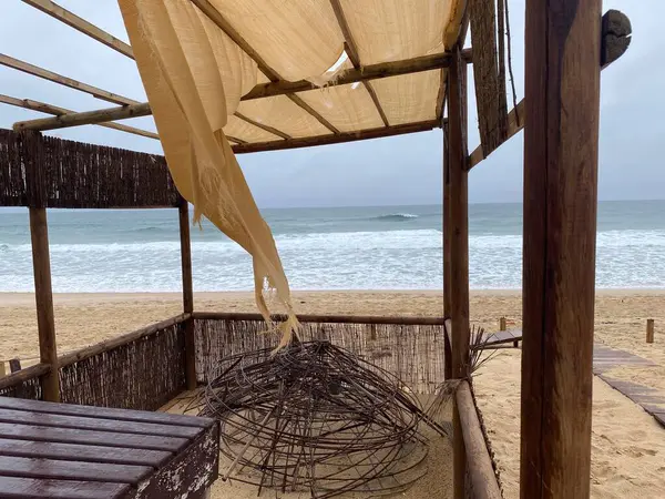 Bej rengi paçavralar rüzgarda dalgalanıyor, bulutlu bir gökyüzünün altında yumuşak okyanus dalgaları olan boş bir kumsal. Sönük renkler, aşınmış kumaş, melankolik, nostaljik atmosfer..