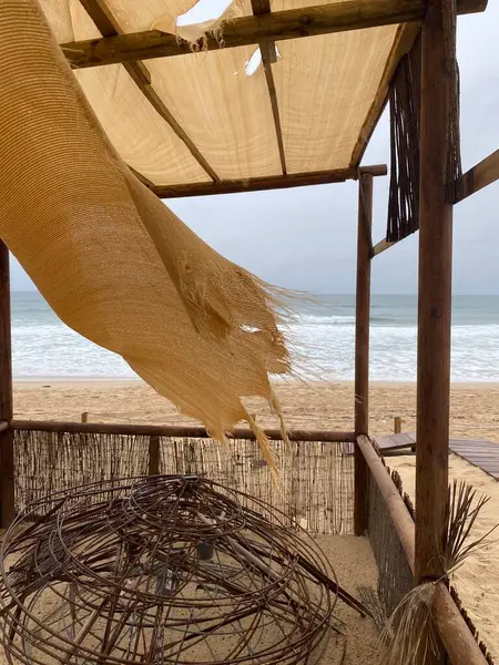 Bej rengi paçavralar rüzgarda dalgalanıyor, bulutlu bir gökyüzünün altında yumuşak okyanus dalgaları olan boş bir kumsal. Sönük renkler, aşınmış kumaş, melankolik, nostaljik atmosfer..