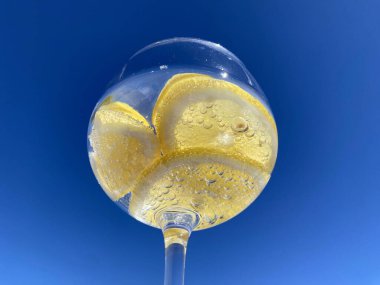 Parlak mavi gökyüzüne karşı limon dilimli, köpüklü narenciye içeceği yakın plan. Meyveye yapışan küçük kabarcıklar taze ve ferahlatıcı hissi arttırır. Yaz, su, sağlıklı içecek.