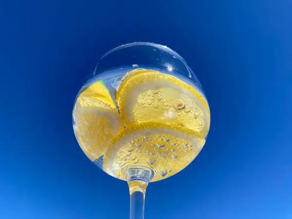 Parlak mavi gökyüzüne karşı limon dilimli, köpüklü narenciye içeceği yakın plan. Meyveye yapışan küçük kabarcıklar taze ve ferahlatıcı hissi arttırır. Yaz, su, sağlıklı içecek.