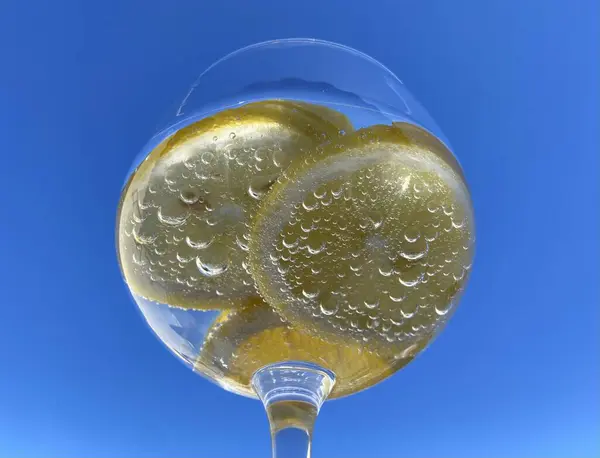 Parlak mavi gökyüzüne karşı limon dilimli, köpüklü narenciye içeceği yakın plan. Meyveye yapışan küçük kabarcıklar taze ve ferahlatıcı hissi arttırır. Yaz, su, sağlıklı içecek.
