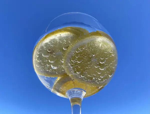 Parlak mavi gökyüzüne karşı limon dilimli, köpüklü narenciye içeceği yakın plan. Meyveye yapışan küçük kabarcıklar taze ve ferahlatıcı hissi arttırır. Yaz, su, sağlıklı içecek.