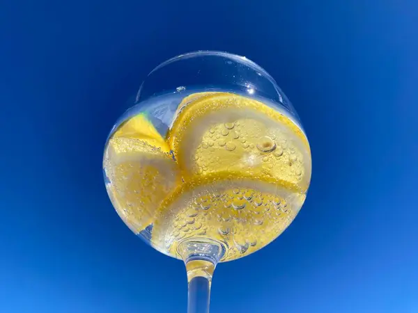Parlak mavi gökyüzüne karşı limon dilimli, köpüklü narenciye içeceği yakın plan. Meyveye yapışan küçük kabarcıklar taze ve ferahlatıcı hissi arttırır. Yaz, su, sağlıklı içecek.
