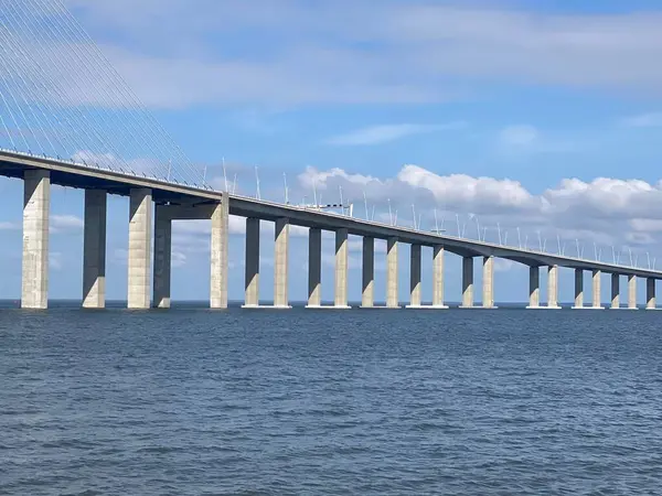 Vasco da Gama Köprüsü nehrin üzerinde yüzerek soyut bir mimari arkaplan oluşturur. Temiz yatay çizgiler, derin mavi su ve minimalist dizayn gökyüzü ve renkli şamandıralarla harmanlanmış..
