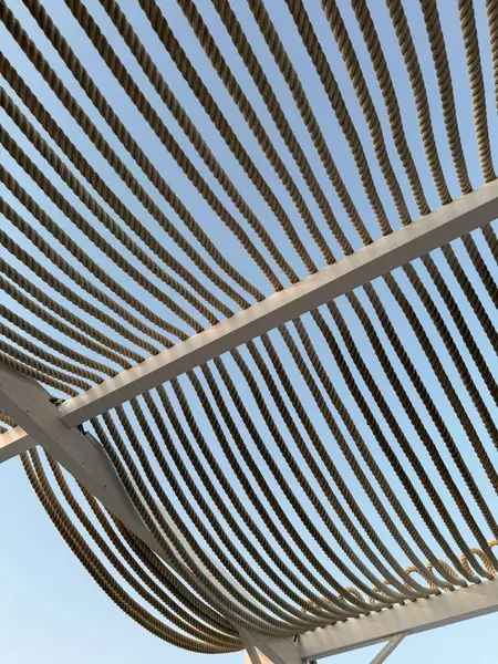 Halat gölgelik yapısı. Metal çerçeveye uzanan paralel halat hatları ile berrak mavi gökyüzüne uzanan modern bir güneş gölgesi yapısının perspektifi. Kafe terasında ya da açık alanda gölgelendirme. 