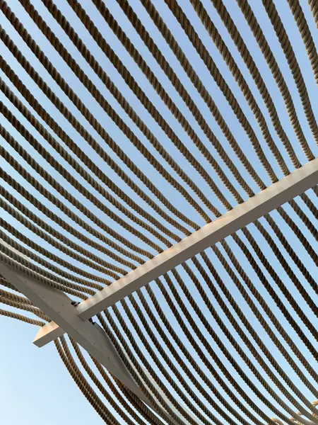 Halat gölgelik yapısı. Metal çerçeveye uzanan paralel halat hatları ile berrak mavi gökyüzüne uzanan modern bir güneş gölgesi yapısının perspektifi. Kafe terasında ya da açık alanda gölgelendirme. 