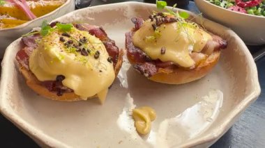 Benedict usulü yumurta, kızarmış ekmeğin üstünde çıtır domuz pastırması, üstüne kremalı hollandez sosu ve mikroyeşillikler, modern seramik bir tabakta servis edilen mükemmel bir brunch..