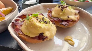 Benedict usulü yumurta, kızarmış ekmeğin üstünde çıtır domuz pastırması, üstüne kremalı hollandez sosu ve mikroyeşillikler, modern seramik bir tabakta servis edilen mükemmel bir brunch..