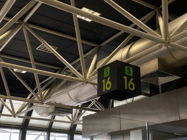 Lizbon Havaalanı terminalinin tavanından sarkan S16 işareti. Borular ve kirişlerle donatılmış sanayi yapısı..
