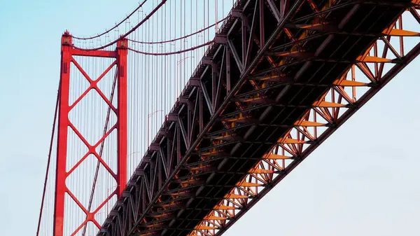 Lizbon, Portekiz 'deki 25 de Abril Köprüsü' nün yakınında. Sert endüstriyel hava, açık kırmızı çelik, soğuk geometri ve soluk gökyüzüne karşı sert çizgiler. Kentsel altyapı estetiği.